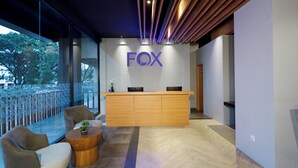 A reception area with a wooden reception desk, two cushioned chairs, and a small table with a plant. - Fox Lite Hotel Cikarang (Cikarang)