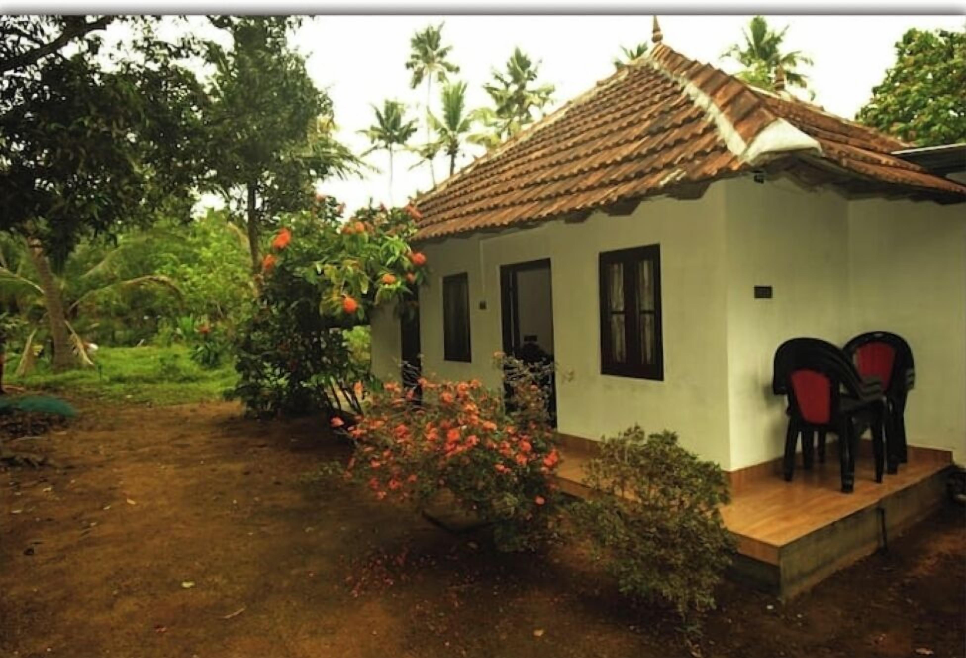 A small house with a tiled roof, a porch with two chairs, and a garden with flowering plants.