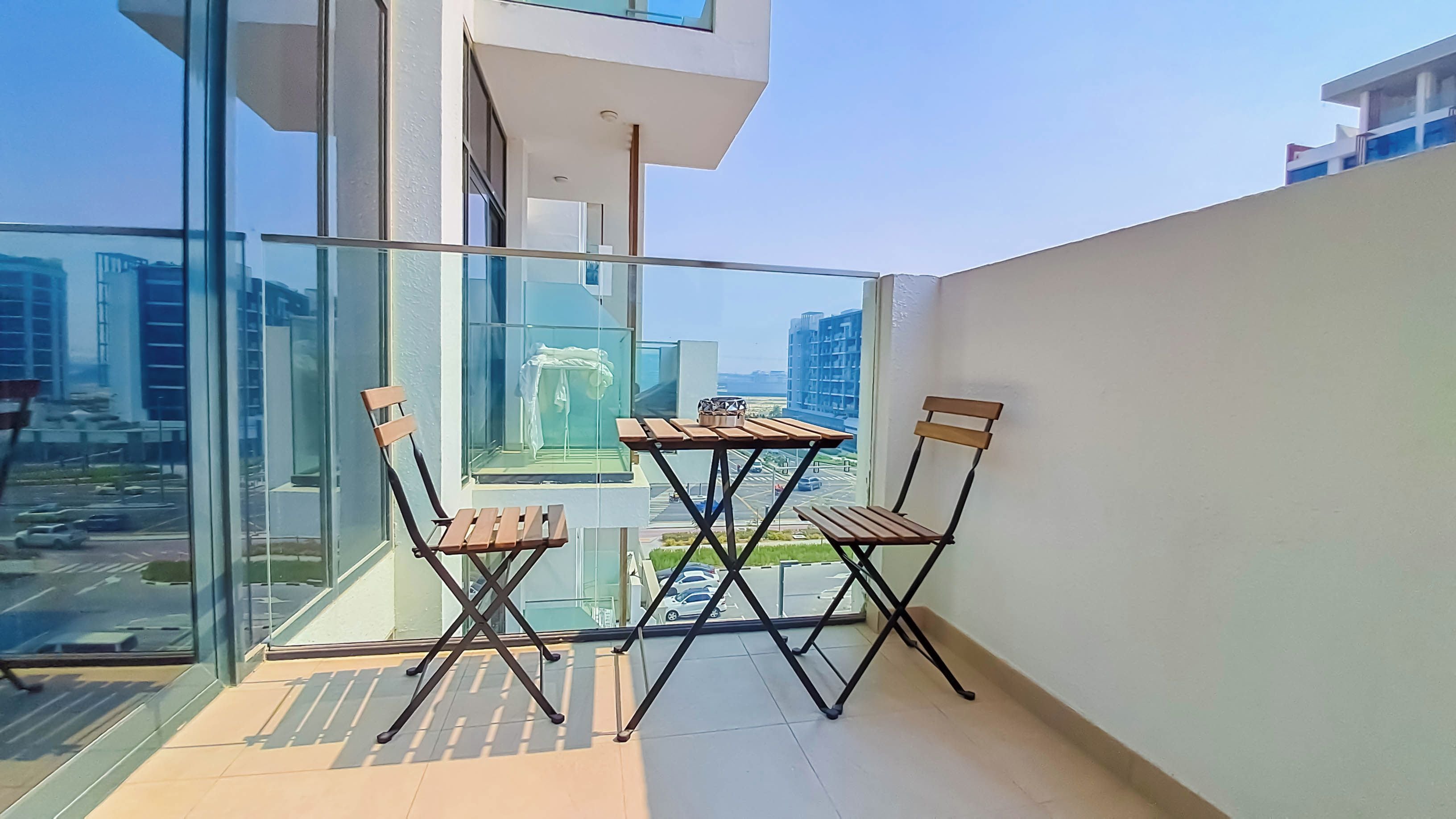 A balcony with a table and two chairs, overlooking a cityscape with tall buildings.