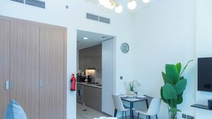 A modern hotel room with a bed, a desk, a chair, a potted plant, a TV, and a kitchen area visible through an open door. - Bloomfields Deluxe STU Azizi Riviera (Dubai)