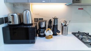 A kitchen with a microwave, toaster, coffee maker, and utensils on the counter. - Bloomfields Deluxe STU Azizi Riviera (Dubai)