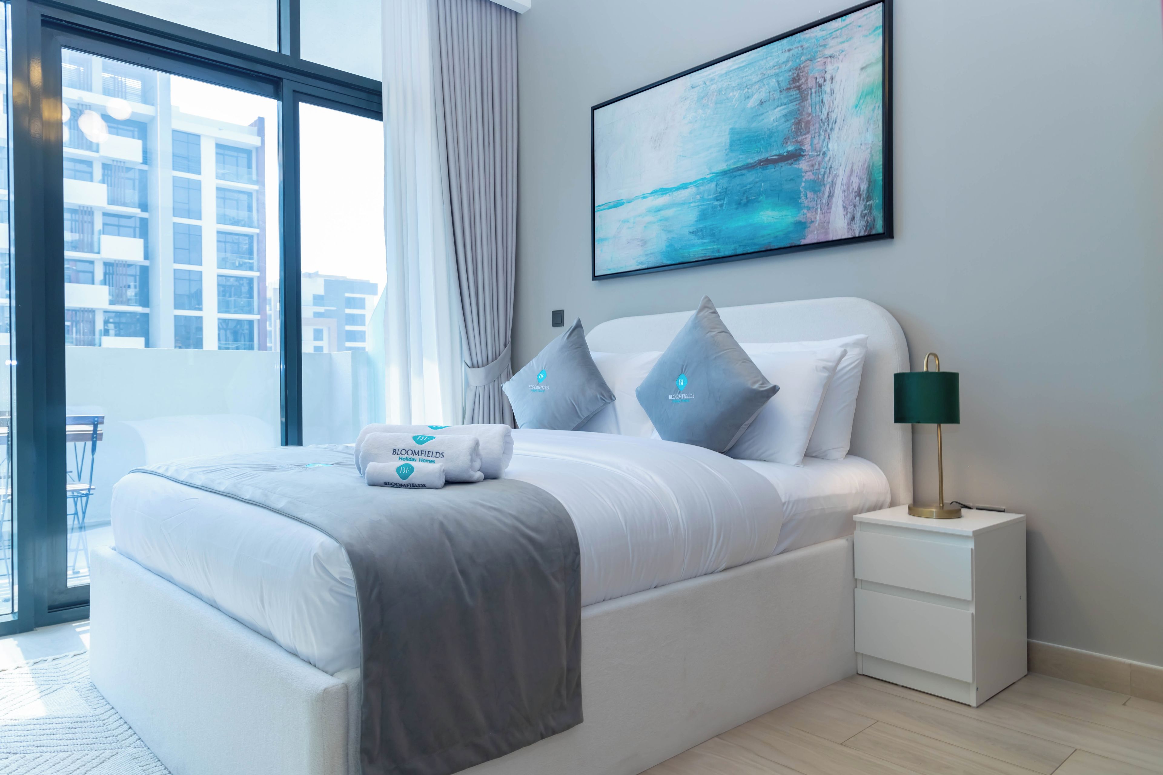 A modern hotel room with a large bed, a nightstand, a lamp, and a painting on the wall.
