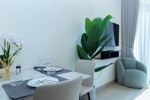 A modern dining area with a table set for two, a large plant, a TV mounted on the wall, and a comfortable armchair. - Bloomfields Studio - Azizi Riviera 19 - Meydan (Dubai)