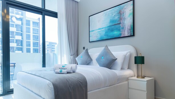 A modern hotel room with a large bed, a nightstand, a lamp, and a painting on the wall. - Bloomfields Deluxe STU Azizi Riviera (Dubai)
