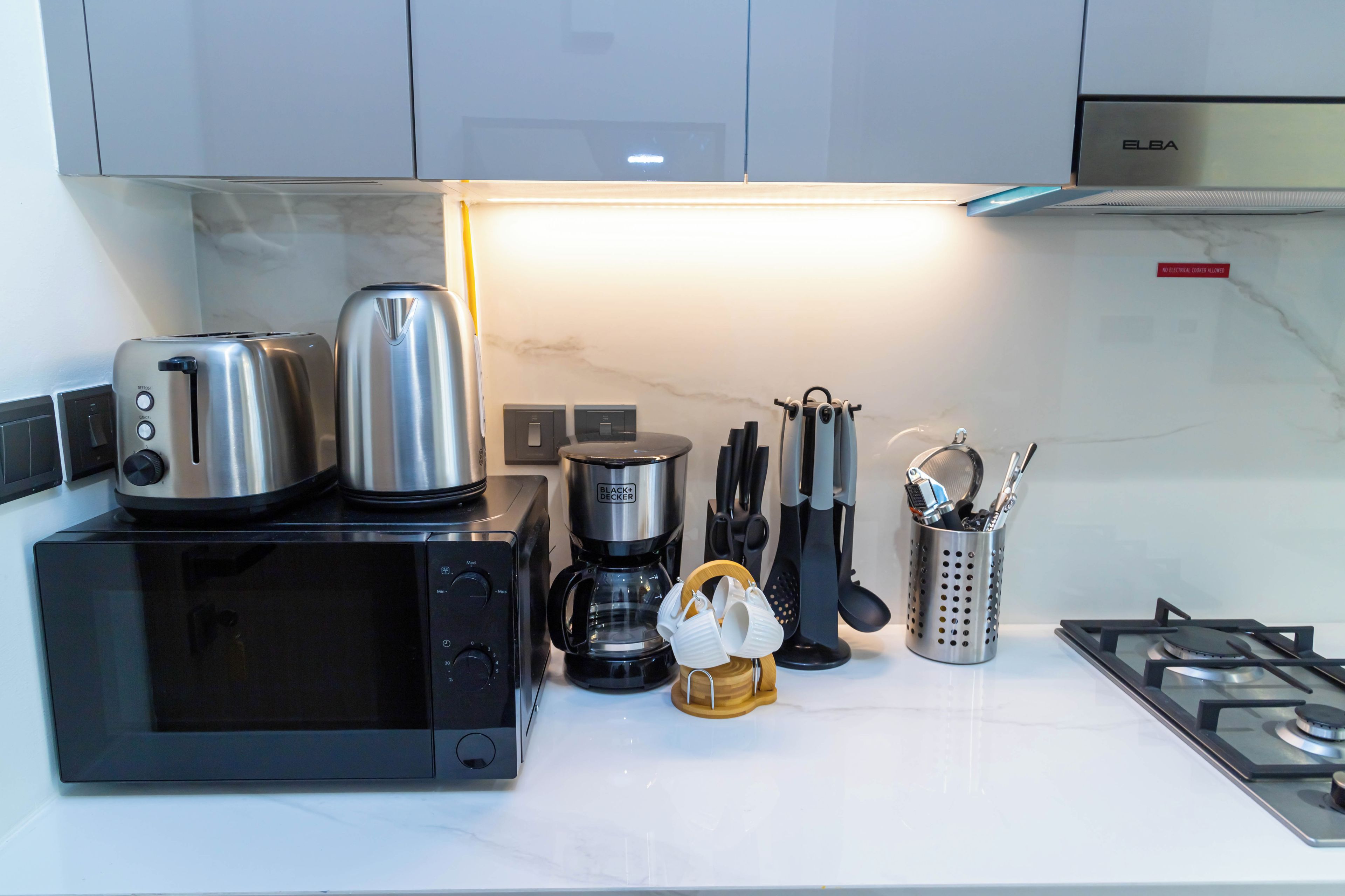A kitchen with a microwave, toaster, coffee maker, and utensils on the counter.