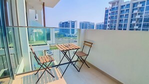 A balcony with a glass partition, two wooden chairs, and a small table. - Bloomfields Deluxe STU Azizi Riviera (Dubai)