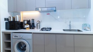 A compact kitchen with a washing machine, microwave, toaster, and a stainless steel range hood. - Bloomfields Deluxe STU Azizi Riviera (Dubai)