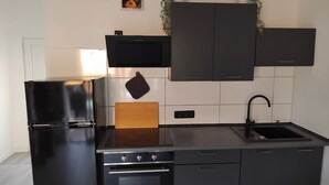 A modern kitchen with black cabinetry, a stainless steel refrigerator, a wooden cutting board, and a black sink. - Cozy bungalow for 4 people in the beautiful Hunsrück (Morbach)