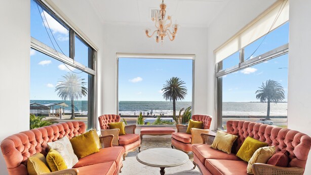 Ein Zimmer mit großem Fenster mit Blick auf einen Strand, ausgestattet mit einem geschnürten Sofa und einem runden Couchtisch.