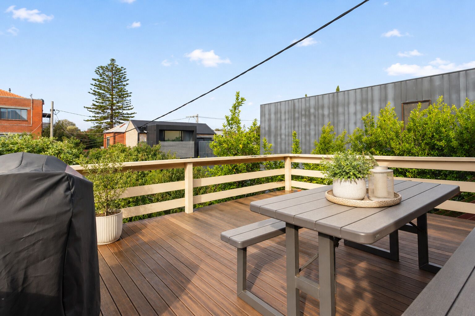 Une terrasse en bois avec une table et des chaises, entourée de verdure et délimitée par une clôture en métal.