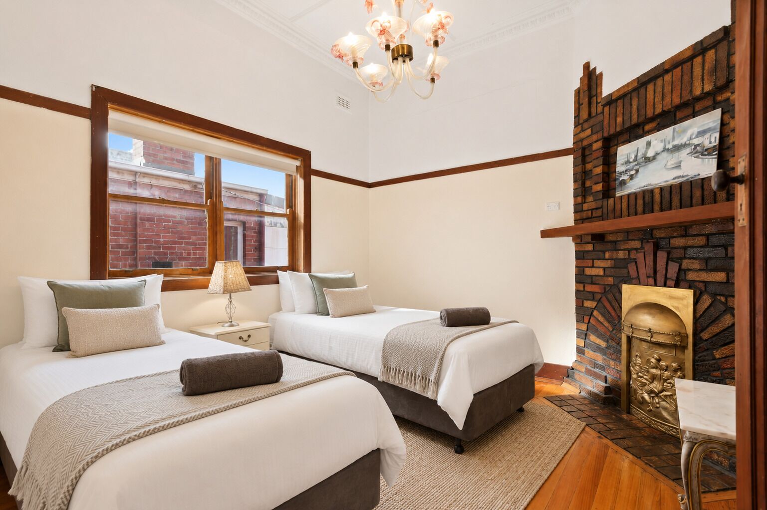 A hotel room with two beds, a fireplace, a window with a view of the city, and a chandelier.