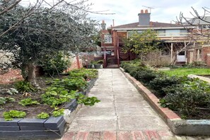 A narrow concrete pathway flanked by brick and stone borders, leading to a residential building with a visible staircase and a gated entrance. - Lisieux by Ready Set Stay (Middle Park)