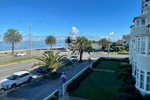 A coastal street with palm trees, a road, and a building with large windows. - Lisieux by Ready Set Stay (Middle Park)