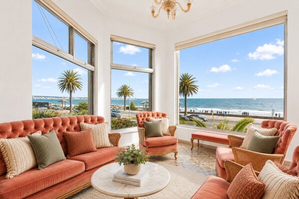 A room with a large window overlooking a beach, furnished with a sofa, chairs, and a coffee table.
