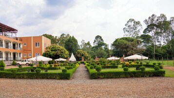 Un jardín bien cuidado con setos ordenados, un sendero de grava y mobiliario exterior con sombrillas.