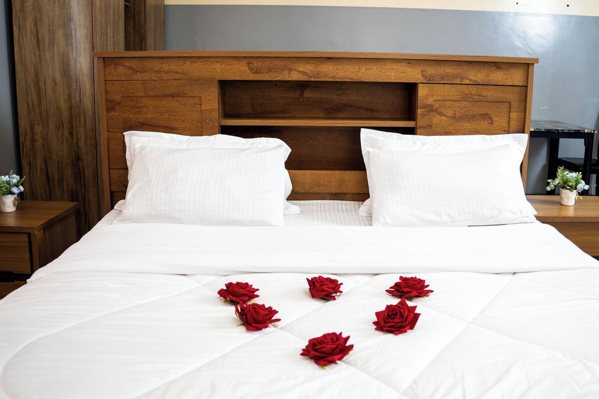 A neatly made bed with white linens and red roses placed on the bed.