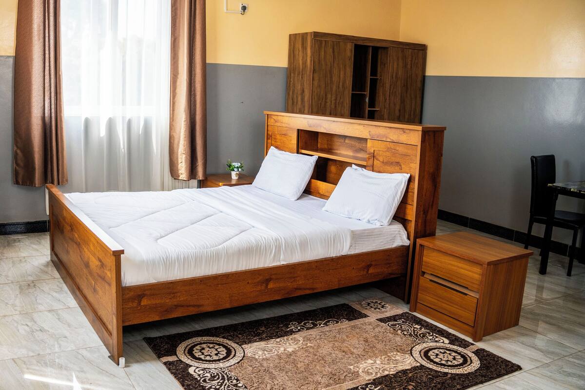 A neatly made bed with a wooden headboard, a bedside table, and a small cabinet.