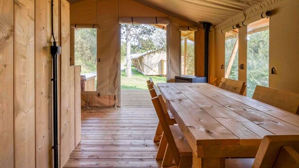 A wooden interior with a large table and benches, a tent-like roof, and a view of the outdoors. - Comet Glamping Tent, Ardennes (Signy-l’Abbaye)
