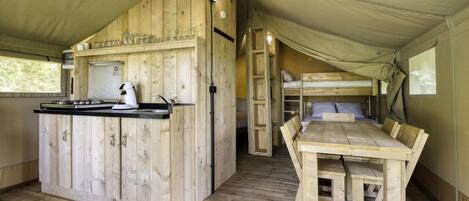 A tented accommodation with a wooden kitchen, a dining table, and a bunk bed.