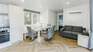 A modern kitchen with white cabinets, a dining table with chairs, a gray sofa, and an air conditioning unit. - Relaxing Apartment With Jacuzzi (Turnhout)