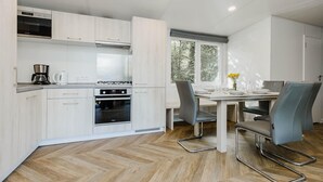 A modern kitchen with white cabinetry, a dining table with chairs, and a window with a view of trees. - Relaxing Apartment With Jacuzzi (Turnhout)