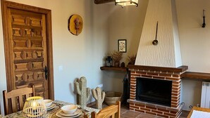 Un coin repas avec une table en bois dressée pour quatre personnes, une cheminée en briques et une porte en bois.