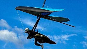 Un parapente en plein vol, avec un ciel bleu dégagé en arrière-plan.