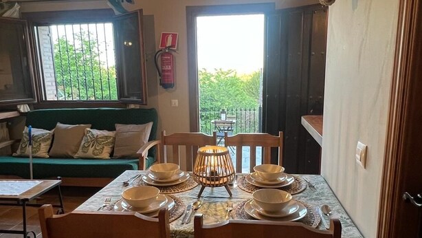 Un coin repas avec une table dressée pour quatre personnes, un canapé vert et une vue sur le balcon.
