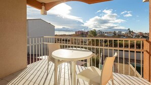 Un balcón con una mesa y sillas blancas, vistas a un paisaje urbano y una piscina al fondo.