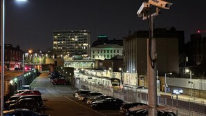 A nighttime urban street scene with parked cars, a pedestrian bridge, and buildings with illuminated windows. - Exquisite 1 Bedroom (Orpington)