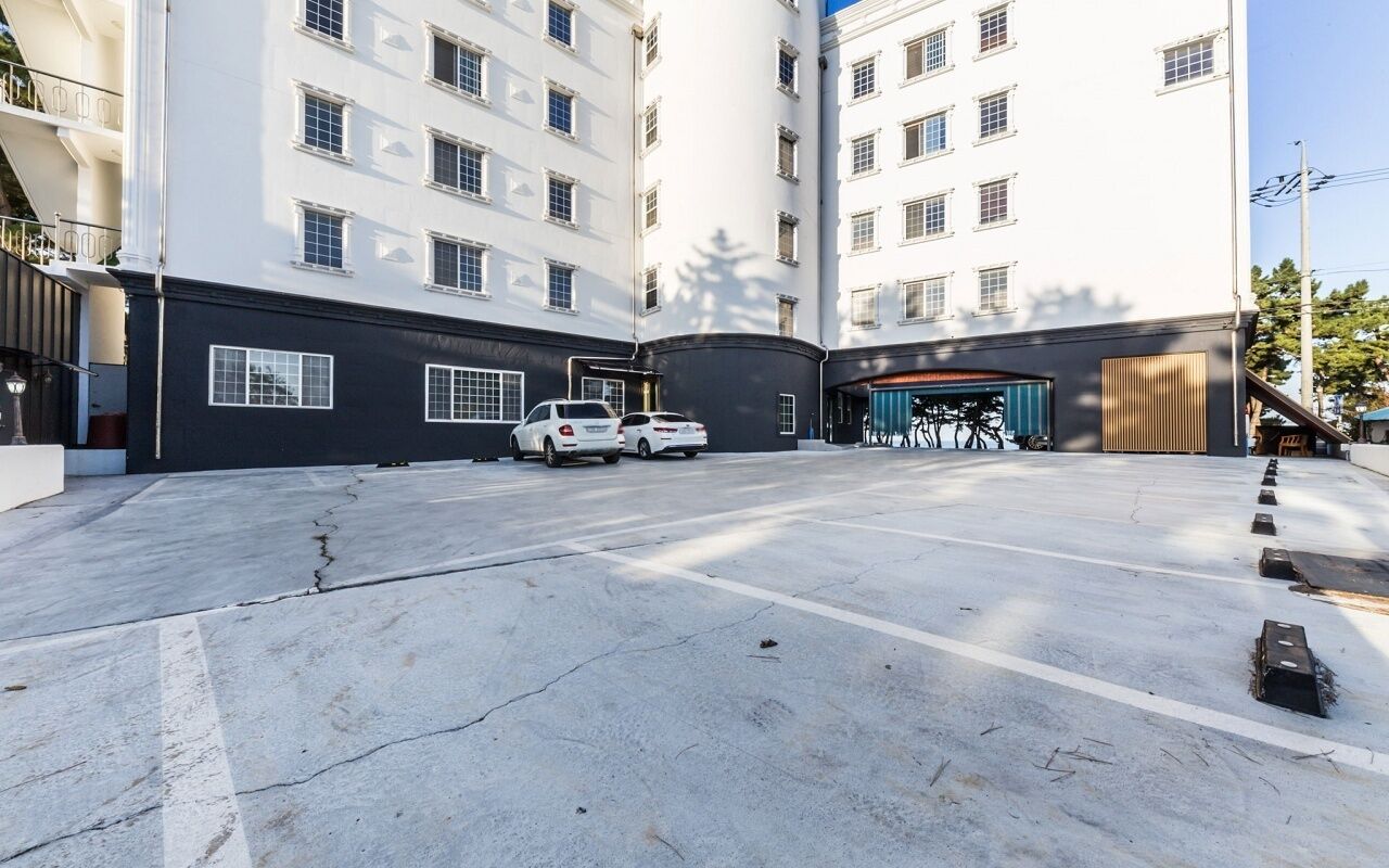A parking area with two white cars, a building with multiple windows, and a covered area with bicycles.