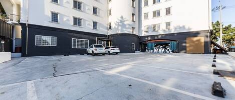 A parking area with two white cars, a building with multiple windows, and a covered area with bicycles.