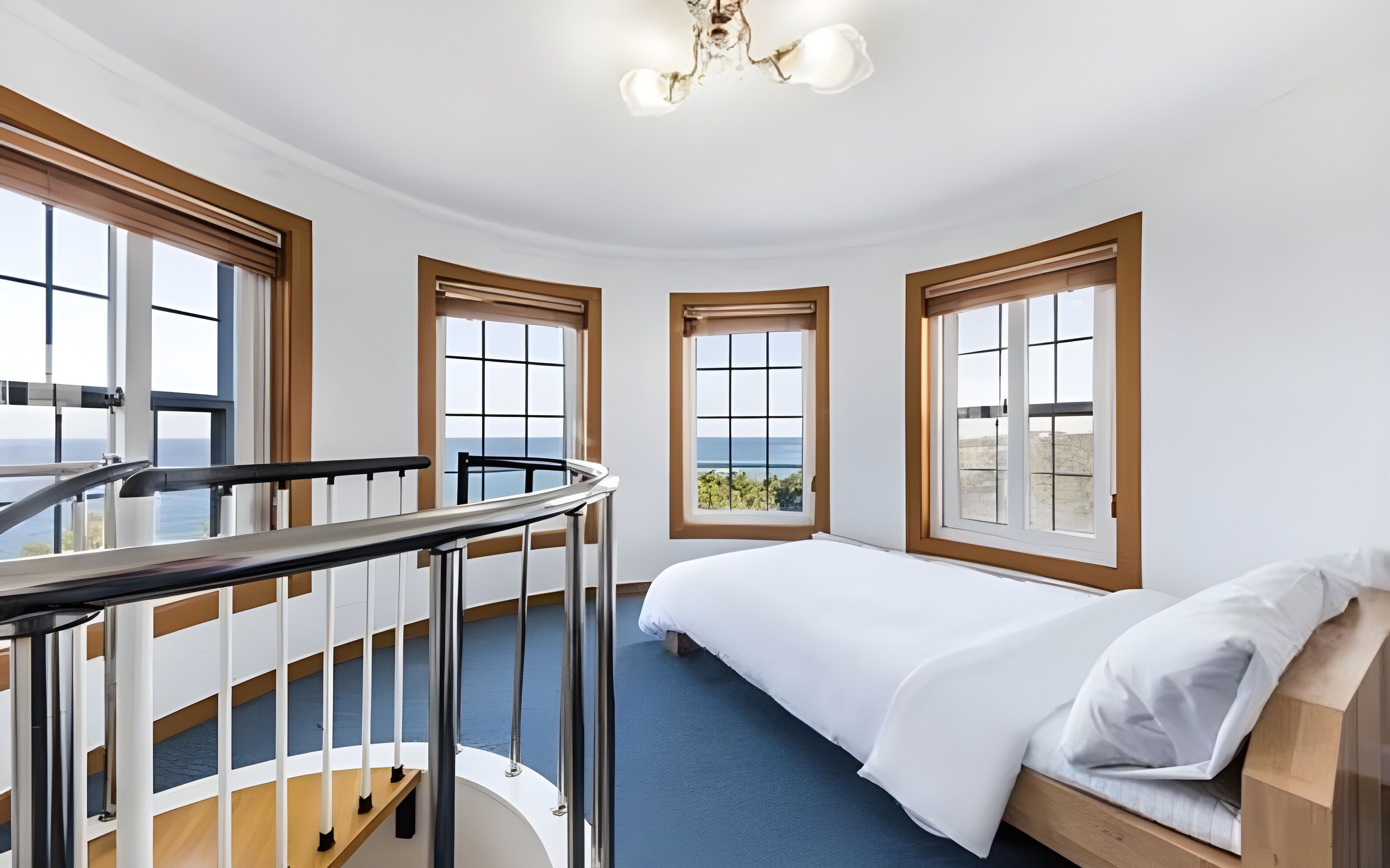 A bedroom with a bed, a view of the sea, and a balcony with a railing.