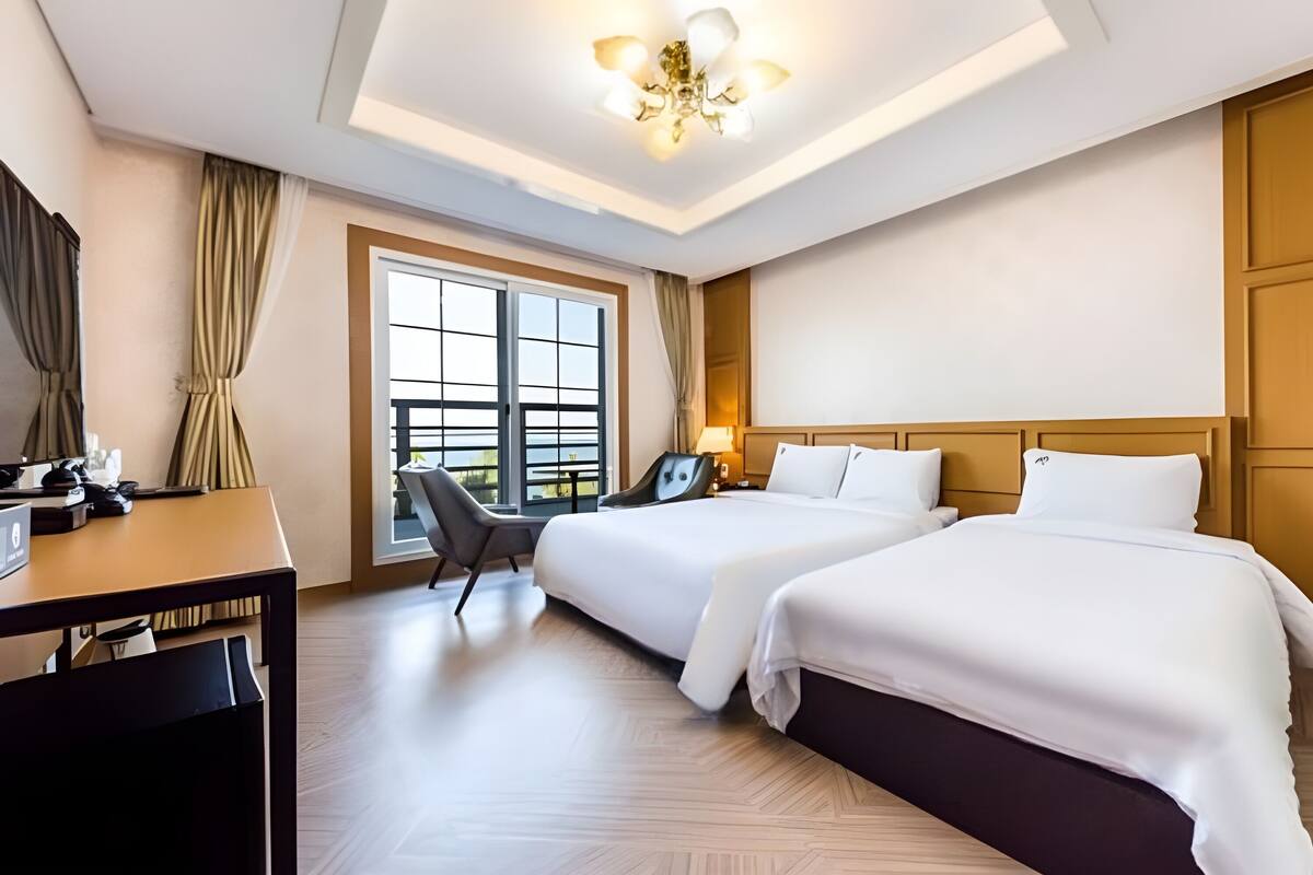 Habitación de hotel con dos camas, un escritorio, una silla, una ventana con vistas y una lámpara en el techo.