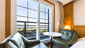 Une chambre d’hôtel avec un balcon, une petite table, deux fauteuils en cuir et un lit.