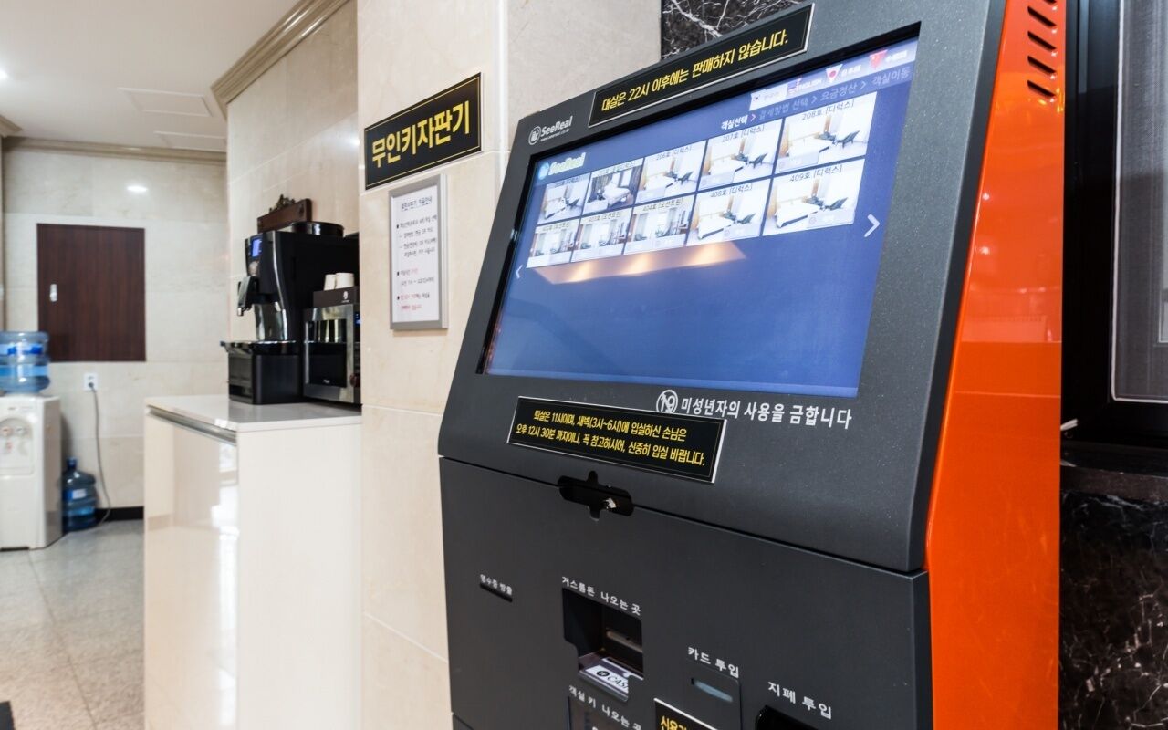 A self-service kiosk with a digital display, a coffee machine, and a water dispenser in a hotel lobby.