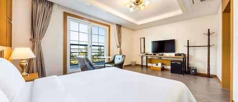 A hotel room with a large bed, a desk, a chair, a TV, and a balcony with curtains.