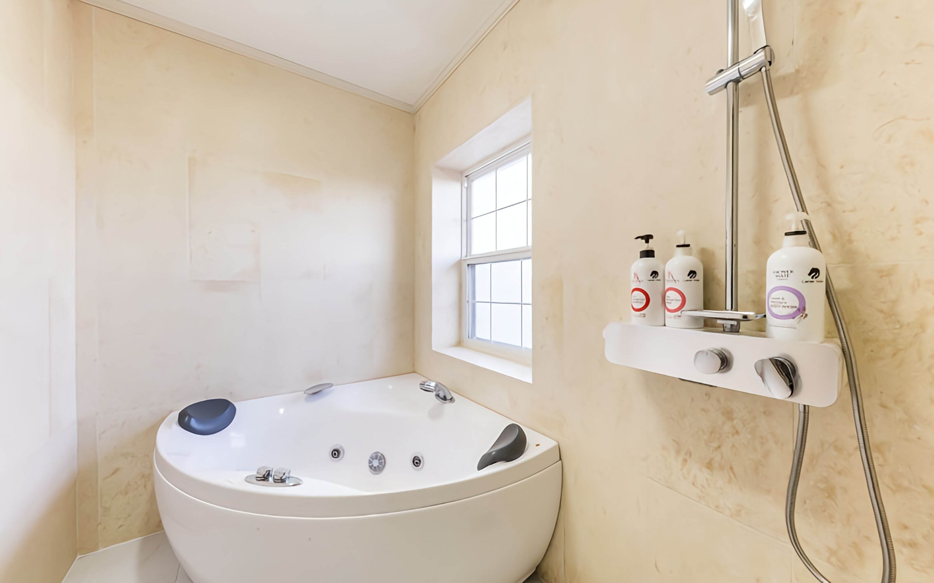 Un baño con una bañera grande, una ventana y una zona de ducha con artículos de aseo.