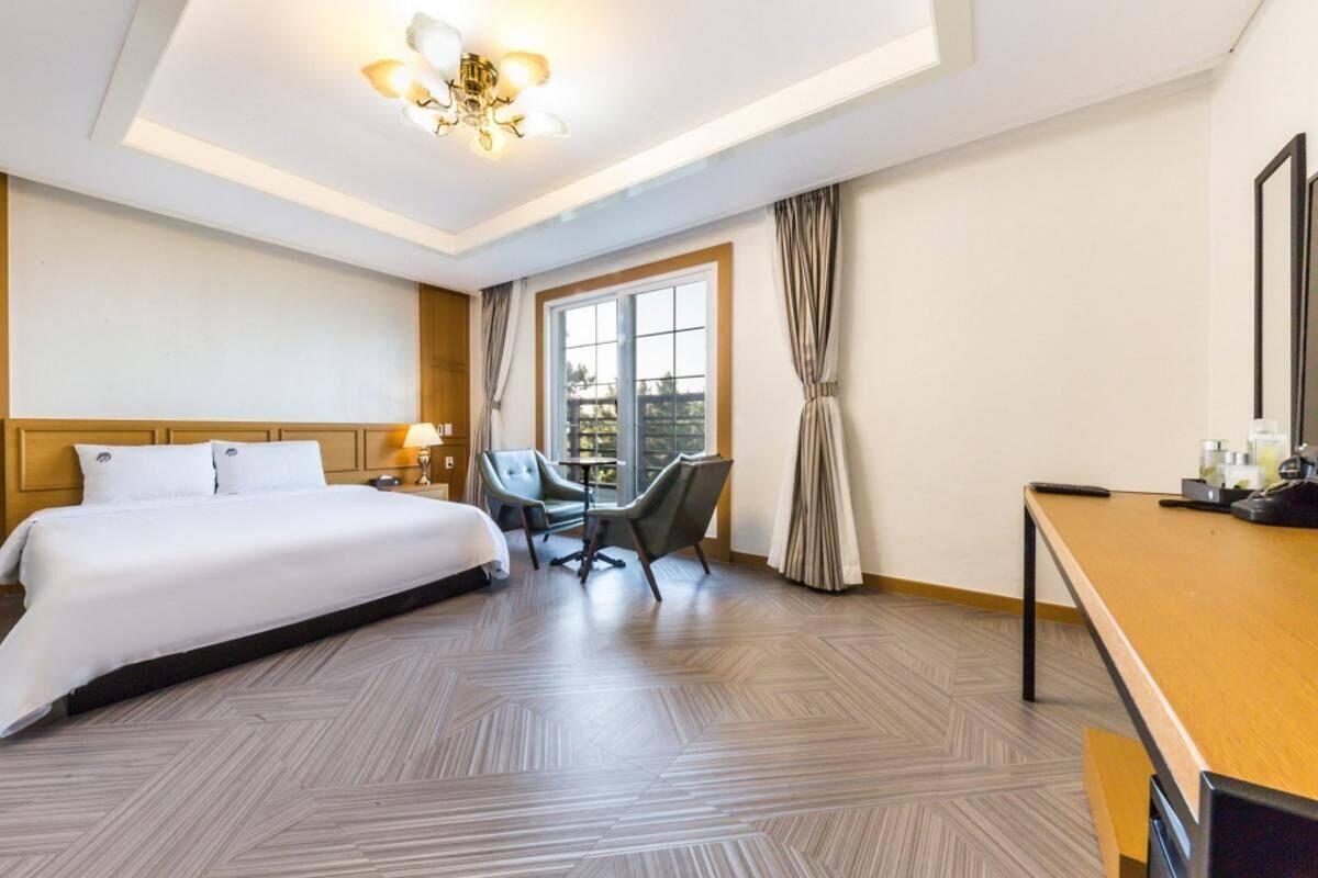 Una habitación de hotel con una cama grande, un escritorio, una silla y un ventanal con cortinas.
