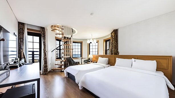 Une chambre d’hôtel avec deux lits, un bureau, une chaise, un escalier et de grandes fenêtres.