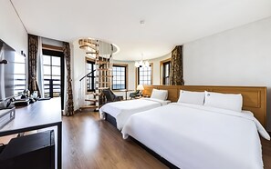 A hotel room with two beds, a desk, a chair, a staircase, and large windows.