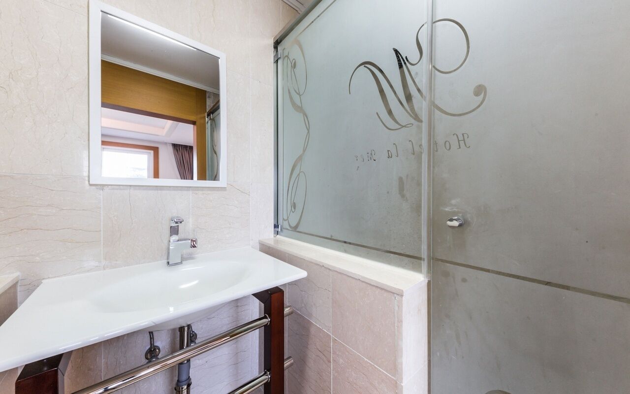 Un baño con un lavamanos blanco, un espejo y una puerta de ducha de vidrio con una inscripción decorativa.
