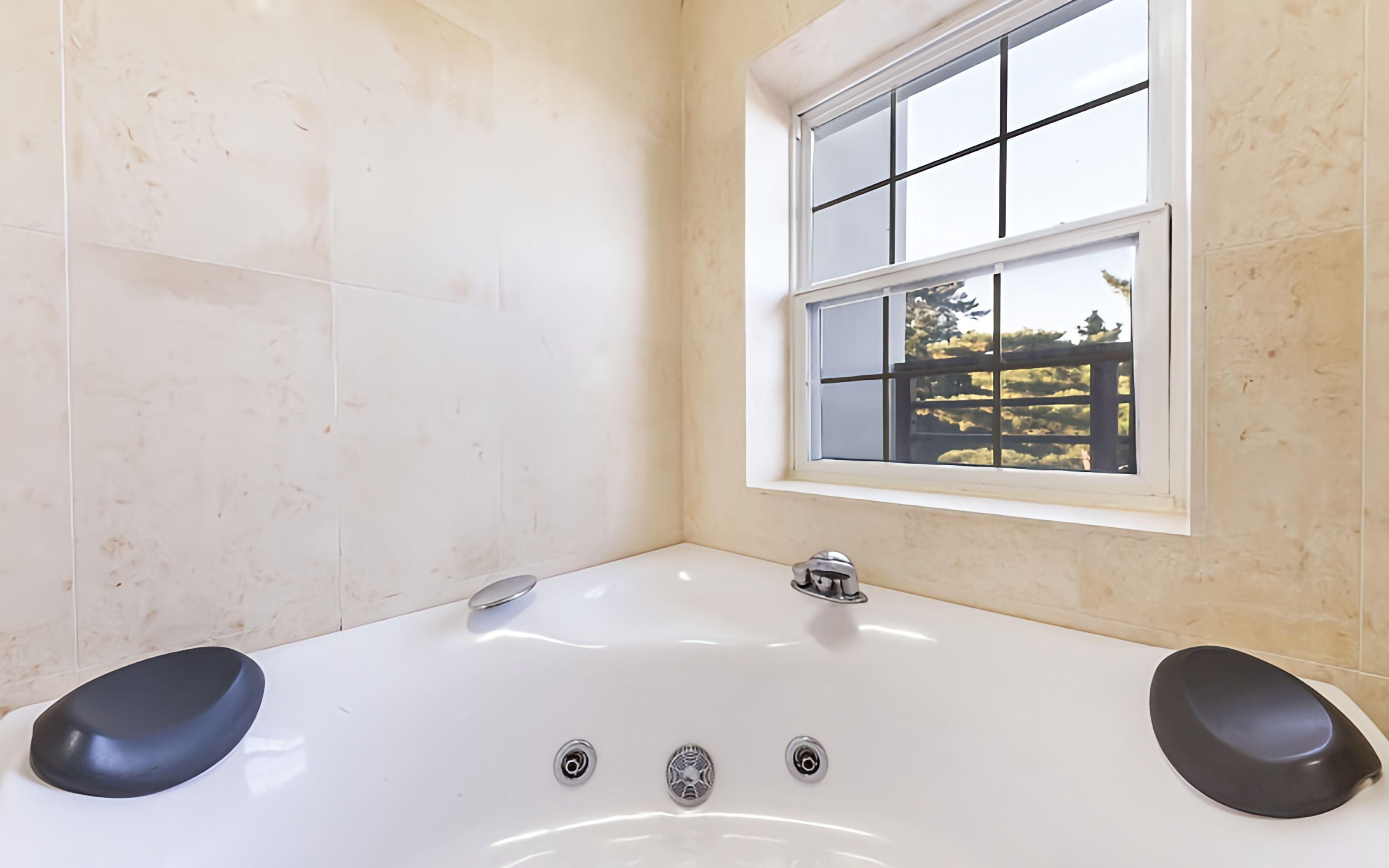 Un baño moderno con una bañera grande, una ventana con vistas a zonas verdes y una pared revestida de azulejos.