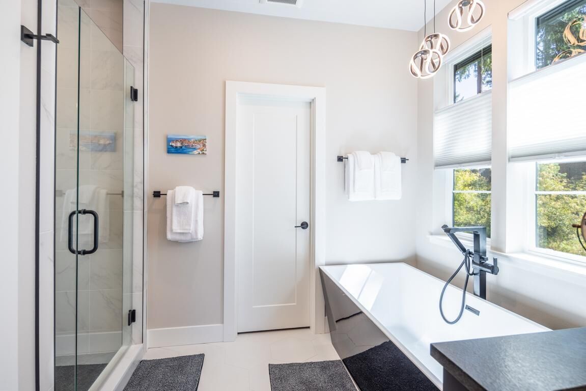 Un baño moderno con cabina de ducha de vidrio, bañera y ducha de mano, además de una puerta con toallero.