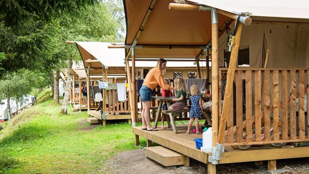 A row of wooden cabins with a covered porch, a table, and a bench. - Terrace Apartment with Forest (Dochamps)