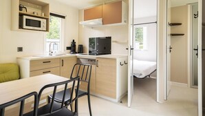 Eine kompakte Küche mit Mikrowelle, Herd und Kühlschrank, ein Essbereich mit Tisch und Stühlen sowie ein Bett in einem separaten Zimmer.