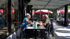 Ein Straßencafé mit Tischen, Stühlen, Sonnenschirmen und Blumentöpfen.