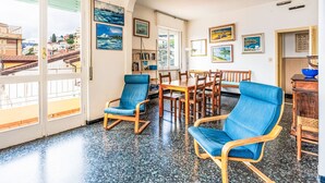 Une pièce spacieuse comprenant un coin repas, un coin salon avec des chaises bleues et une vue sur la ville grâce à de grandes fenêtres.