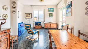 Un coin repas avec une table et des chaises en bois, un canapé bleu et un téléviseur posé sur un meuble en bois.