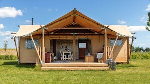 Une grande tente ouverte sur l’extérieur, dotée d’une terrasse en bois et d’une table installée devant.